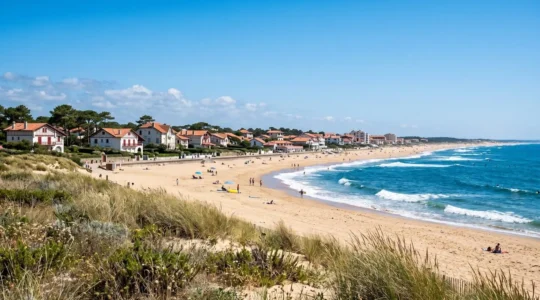 Vue ensoleillée de la plage d'Hossegor avec architecture landaise typique en arrière-plan, ciel bleu éclatant et sable doré